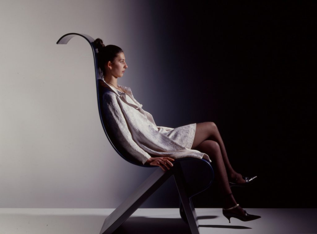 Woman is sitting on wave-formed chair.