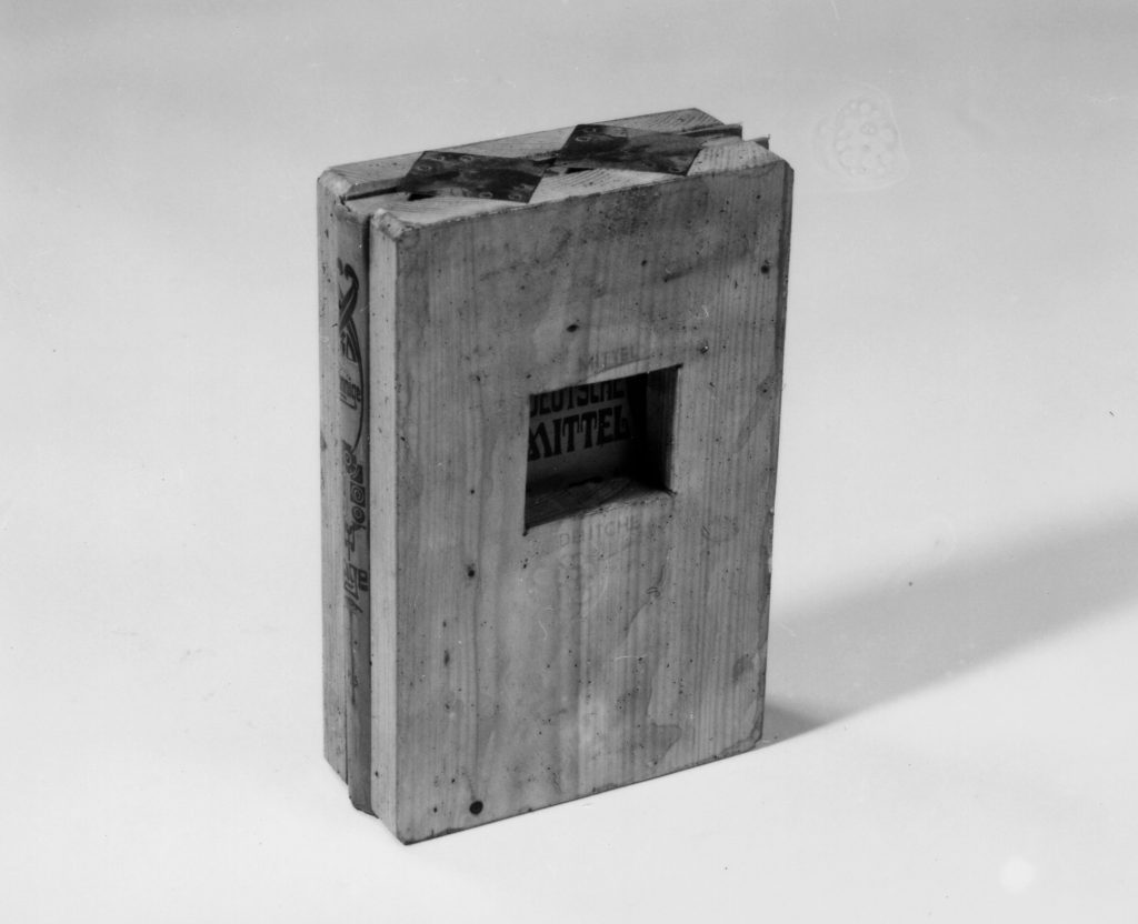 A book in between 2 small wodden boards nailed together. A cutted out hole in the wooden board to read the book title.