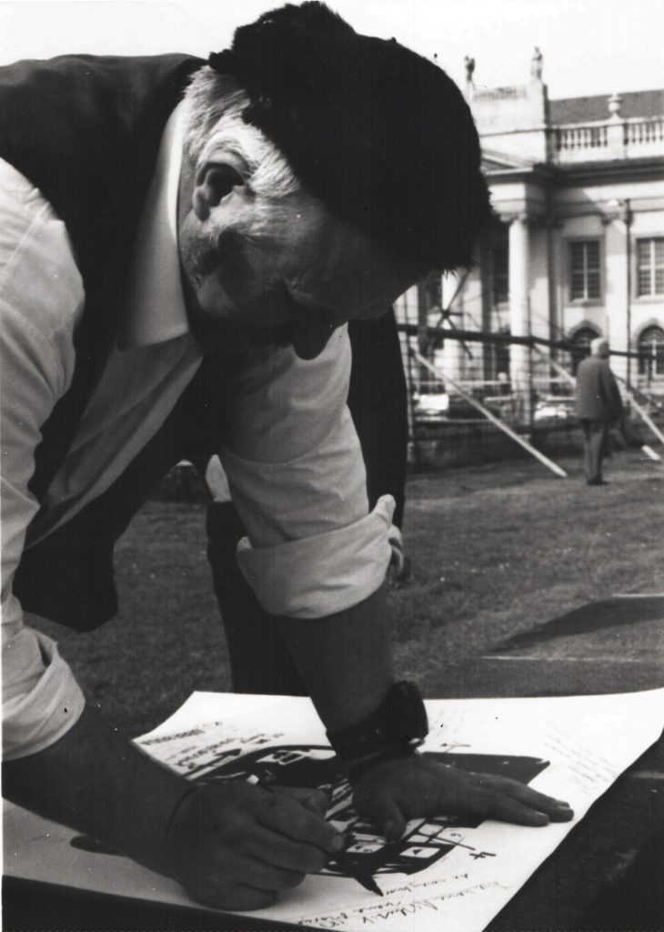 Man writes on large white sheet with collages.